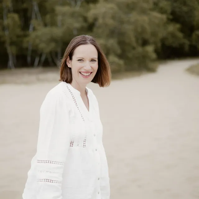 Frau in weißer Bluse lächelt bei einem Portraitshooting am Strand
